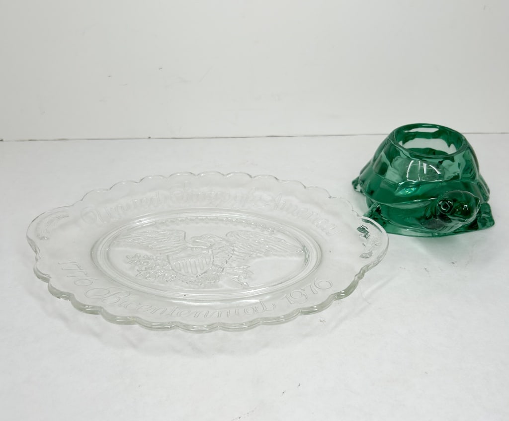 TWO PIECES OF PRESSED GLASS, 1976 AND LATER: An oval clear pressed glass commemorative plate celebrating the American Bicentennial. The central well features a relief-molded spread-winged eagle holding a shield above a ribbon motif. The
