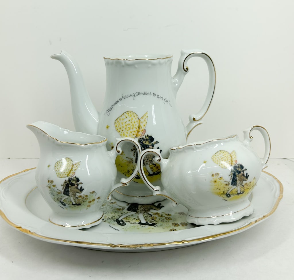 HOLLY HOBBIE PORCELAIN TEA SET 1973: Japanese porcelain tea set featuring Holly Hobbie illustrations produced by World Wide Arts, Inc. in 1973. Each piece features a transfer-printed graphic with gilded rims and is marked on the undersid
