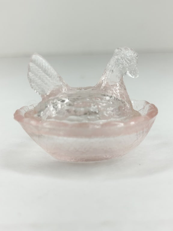 MINIATURE PINK GLASS HEN ON NEST: A two-piece miniature covered dish in the form of a hen on a nest, featuring a clear pressed glass body with a faint pink tint applied to the rims and raised features. The lid depicts a stylized hen w