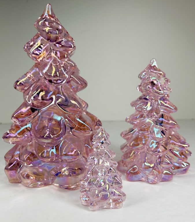 MOSSER TRIO OF IRIDESCENT PINK GLASS CHRISTMAS TREES: A set of three stylized Christmas tree figurines crafted in translucent pink glass. Each tree features a tiered, bubbled form finished with an iridescent carnival coating. No maker marks or signatures