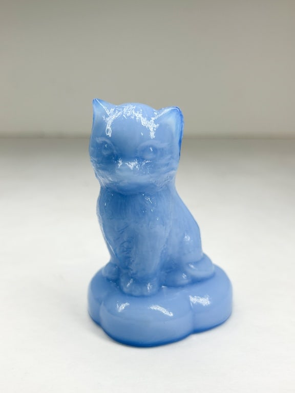 BOYD BLUE SITTING KITTEN ON PILLOW: Pressed glass figurine of a seated kitten on a scalloped base, executed in light blue slag glass with white opalescent marbling. The rear of the base features an impressed diamond-shaped mark containi