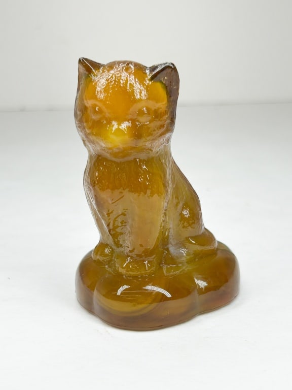 BOYD AMBER SITTING KITTEN ON PILLOW: A pressed slag glass figurine of a seated cat featuring a marbled amber and golden-yellow color palette. The reverse of the base bears an impressed diamond containing a capital letter B, representing 