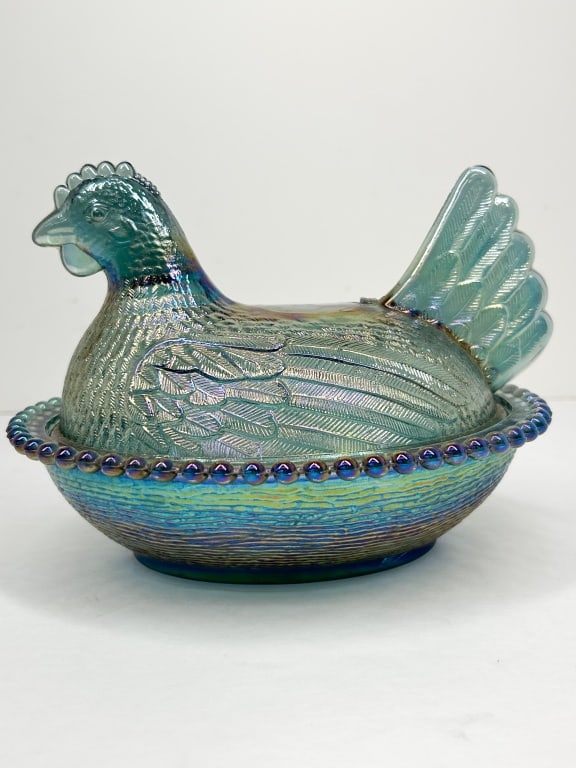 INDIANA IRIDESCENT BLUE GLASS HEN ON NEST: A pressed carnival glass covered dish in the form of a hen on a nest, featuring a teal blue base color with a strong multicolored iridescent finish. The lid is molded as a nesting hen with detailed pl