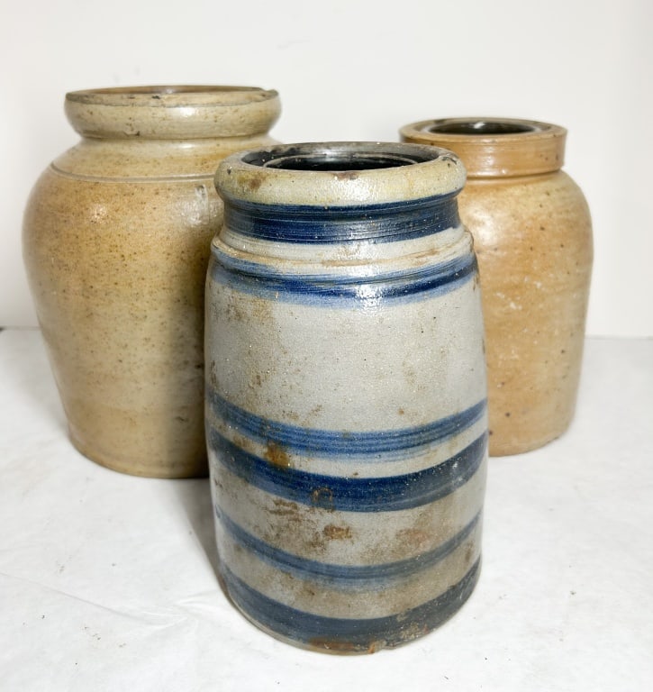 THREE AMERICAN SALT-GLAZED STONEWARE JARS: A trio of American salt-glazed stoneware storage jars featuring Albany-slip glazed interiors. The group includes one cylindrical canning jar decorated with horizontal cobalt blue bands and two ovoid-f