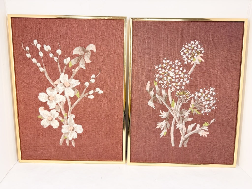 VINTAGE FLORAL CREWEL EMBROIDERY PAIR: A pair of vintage floral crewel embroideries featuring wool thread on a reddish-brown linen support. The needlework depicts white blossoms and budding branches, stretched over oriented strand board