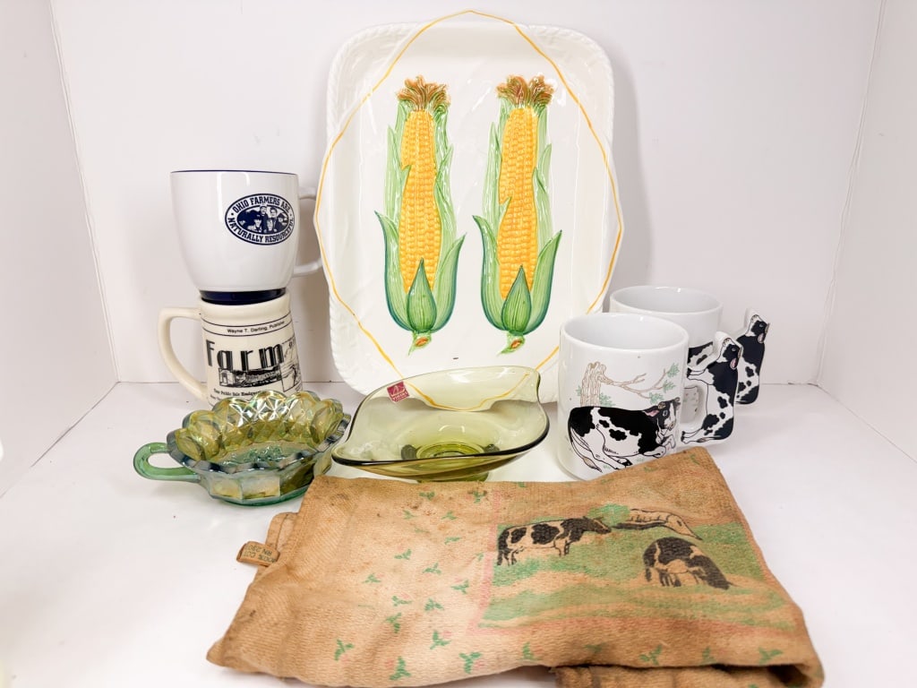 GROUP OF FARM THEMED KITCHENWARE AND TEXTILES: A collection of farm-themed kitchenware including ceramic corn-on-the-cob serving platters, various graphic mugs, and green art glass dishes. A leaf-shaped glass bowl bears a red rectangular label rea