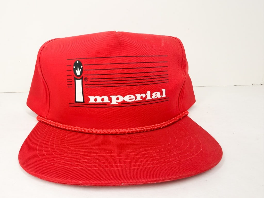 IMPERIAL VINTAGE RED SNAPBACK CAP: A red synthetic fabric trucker-style hat featuring a braided rope detail across the visor and a plastic snapback closure. The front panel bears a screen-printed graphic including horizontal black