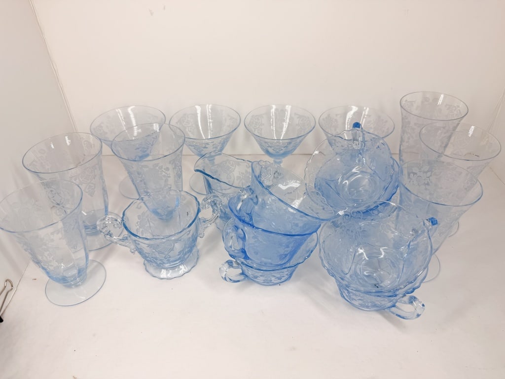 FEDERAL GLASS MADRID PATTERN AZURE BLUE GLASSWARE: A collection of light blue transparent glassware featuring the Madrid pattern, characterized by molded floral motifs, scrollwork borders, and central medallions. The underside of the base on the cups