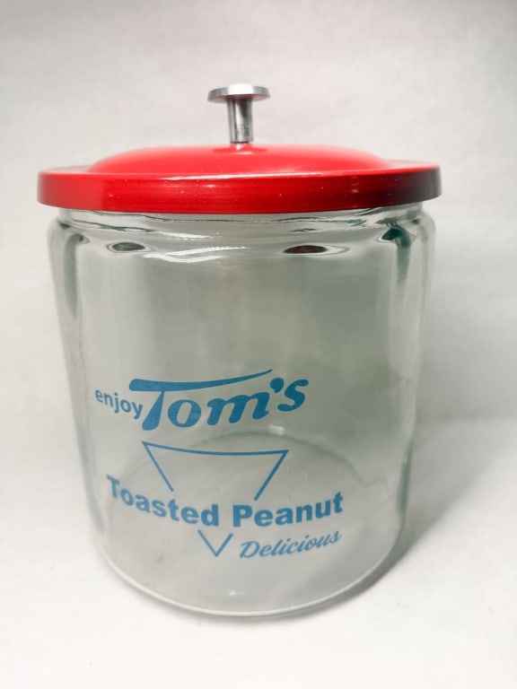 TOM'S TOASTED PEANUTS GLASS JAR: Vintage countertop snack display jar produced for Tom's. The clear glass body features blue applied color lettering reading enjoy Tom's Toasted Peanut V Delicious, with a red painted metal lid and sil