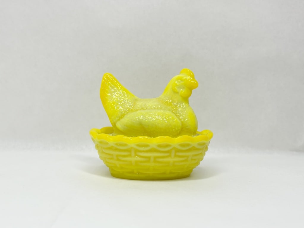MOSSER YELLOW MILK GLASS HEN ON NEST: A two-piece covered dish in opaque yellow milk glass, designed as a sitting hen atop a basketweave base. The glass exhibits an orange-yellow glow under ultraviolet light (image 10).