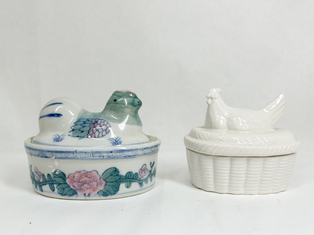 TWO CERAMIC HEN ON NEST TRINKET BOXES: A pair of small ceramic figural boxes. One box is composed of white glazed porcelain featuring hand-painted overglaze enamels in pink and green with blue line borders and a Greek key motif; the other 
