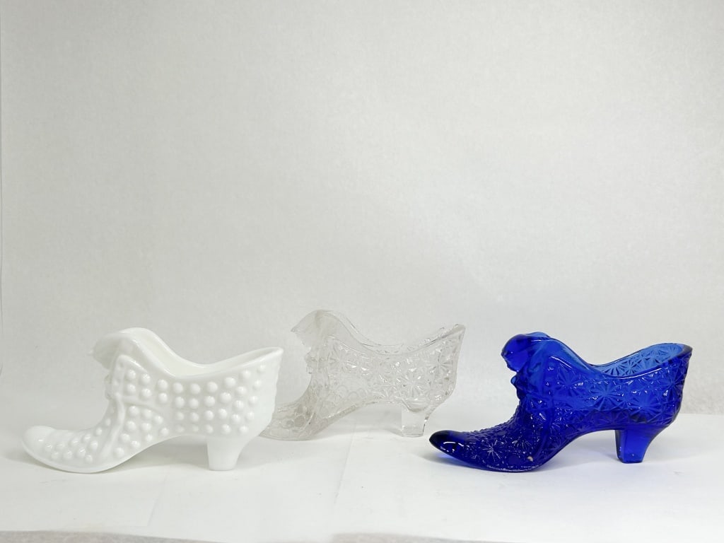 TRIO OF GLASS CAT HEAD SLIPPERS: Three vintage glass high-heel slippers featuring a molded cat head motif on the vamp. The group includes one opaque white milk glass slipper with a hobnail pattern, one clear pressed glass slipper wit