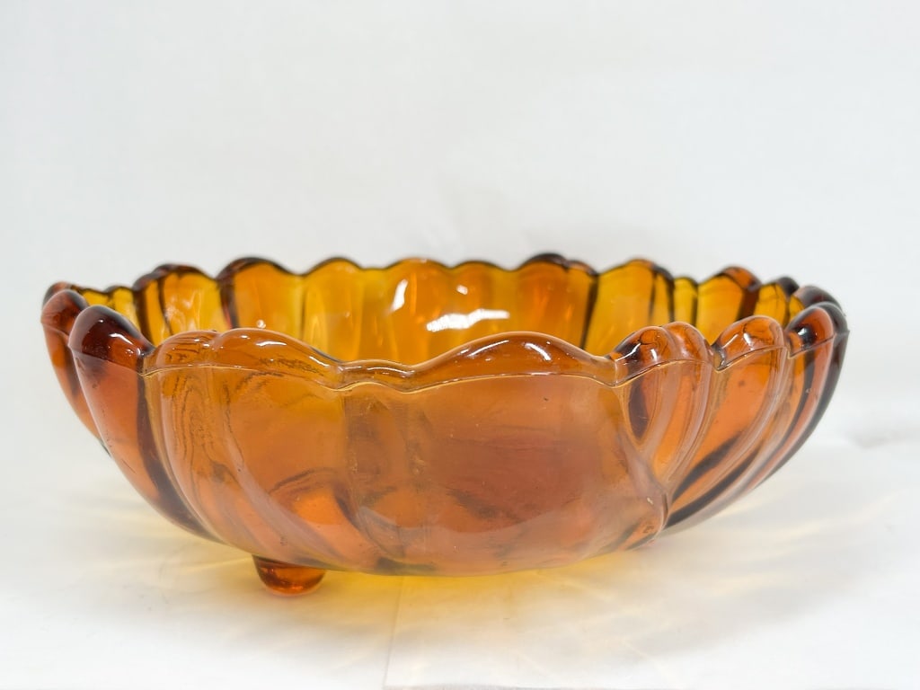 AMBER GLASS SUNFLOWER CENTERPIECE BOWL: A vintage three-footed centerpiece bowl in amber pressed glass, featuring a molded sunflower or sunburst motif to the interior center. The exterior body is formed with broad vertical ribs