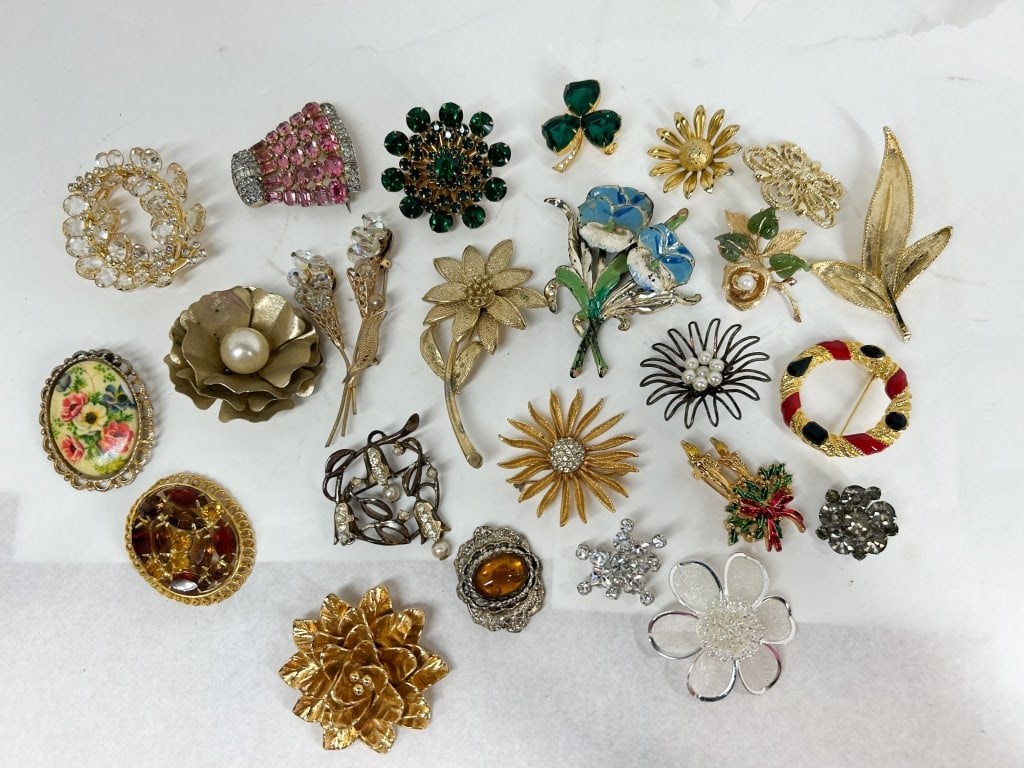 AN ASSORTMENT OF TWENTY-FOUR COSTUME BROOCHES: An assortment of twenty-four costume jewelry brooches in various floral, leaf, and geometric motifs. The collection features gold-tone and silver-tone base metals with accents of pav?-set