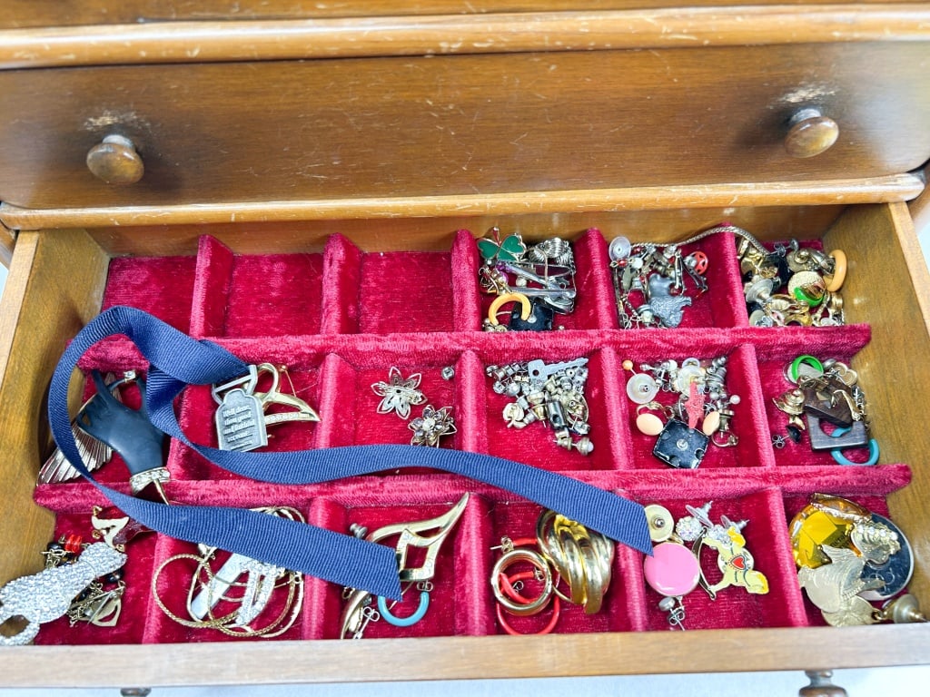 VINTAGE WOODEN JEWELRY CHEST AND COSTUME COLLECTION: A mid-20th-century tabletop miniature chest of drawers constructed from stained wood with turned bun feet and six wooden knobs. The three drawers feature red velvet-flocked interiors with varied