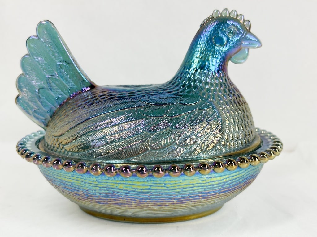 INDIANA IRIDESCENT BLUE CARNIVAL GLASS HEN ON NEST: A two-piece pressed glass covered dish in the form of a nesting hen. The piece features a metallic iridescent finish displaying a spectrum of blue, teal, and violet tones over a medium blue glass
