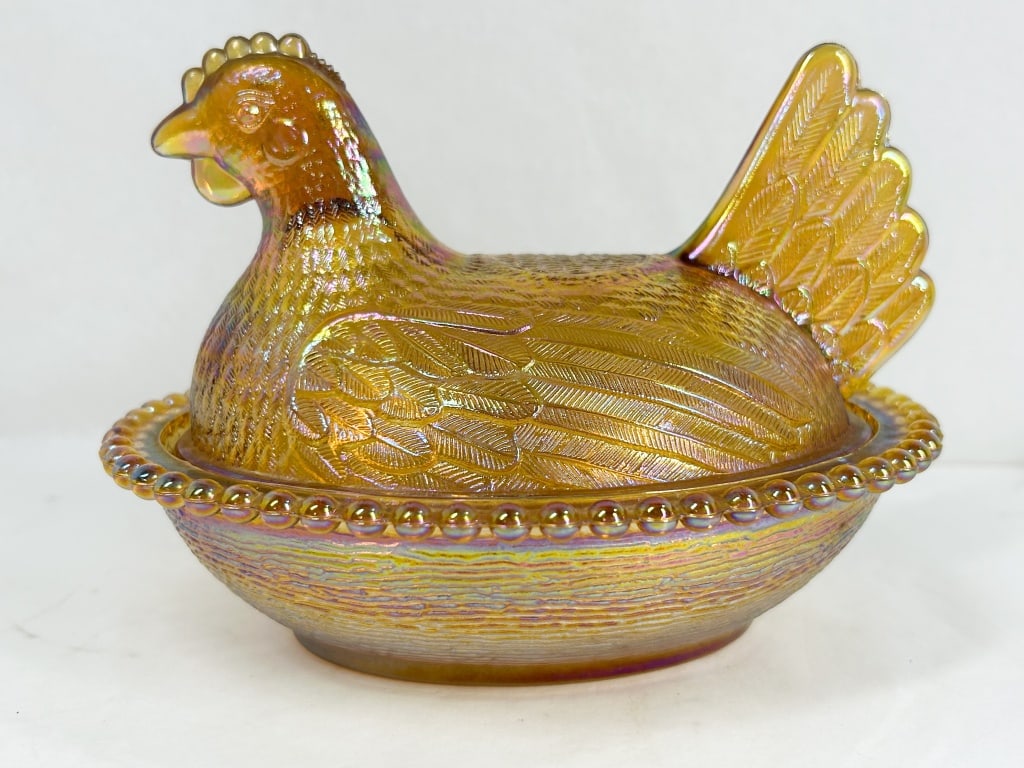 INDIANA IRIDESCENT MARIGOLD CARNIVAL GLASS HEN ON NEST: A two-piece covered dish in the form of a hen on a nest, featuring pressed marigold carnival glass with an iridescent finish. The lid is molded as a hen with detailed feathering and a split tail, whil