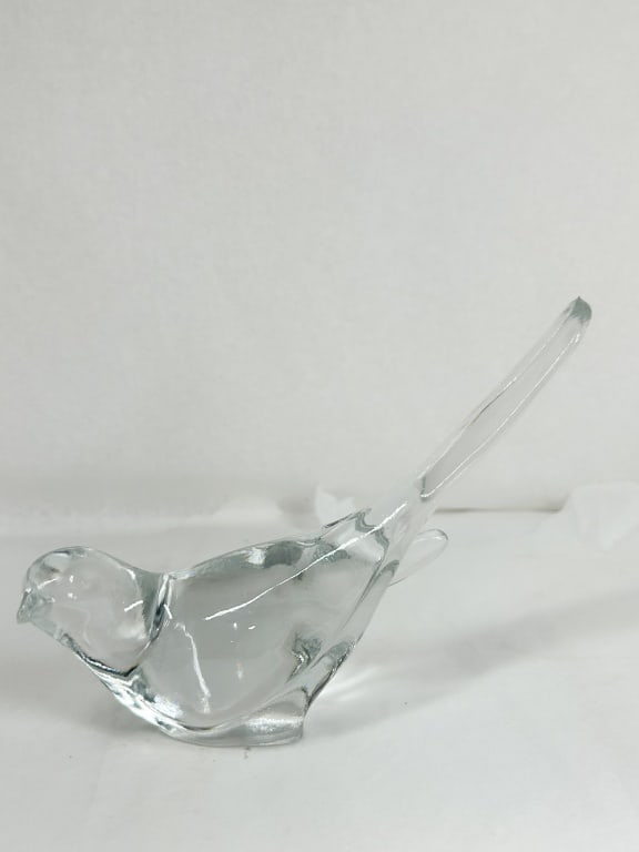 CLEAR GLASS BIRD FIGURINE: A minimalist bird figurine with a rounded body and an elongated, tapering tail. The piece is crafted from solid clear glass and features a flattened base for stability.