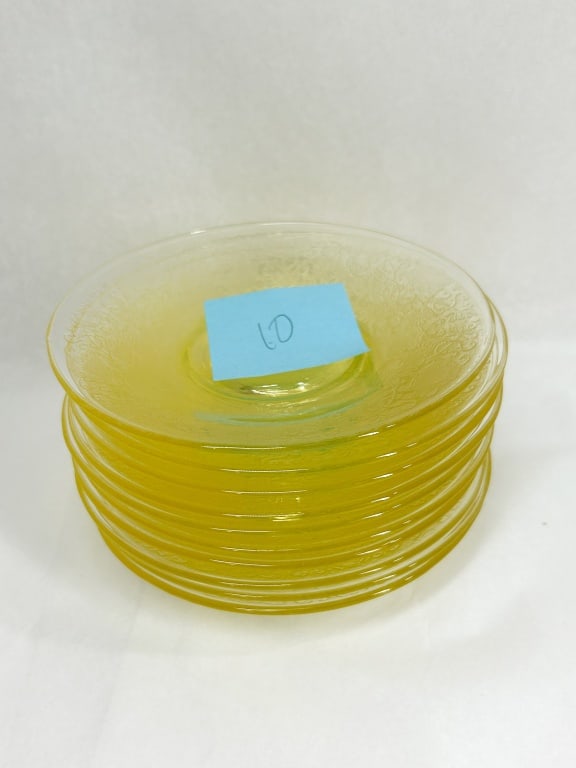 SET OF YELLOW DEPRESSION GLASS SAUCERS: A set of ten yellow pressed glass saucers, dating to the Depression era. The saucers feature an intricate mold-etched floral and scrollwork pattern across the surface, with a smooth central well for a