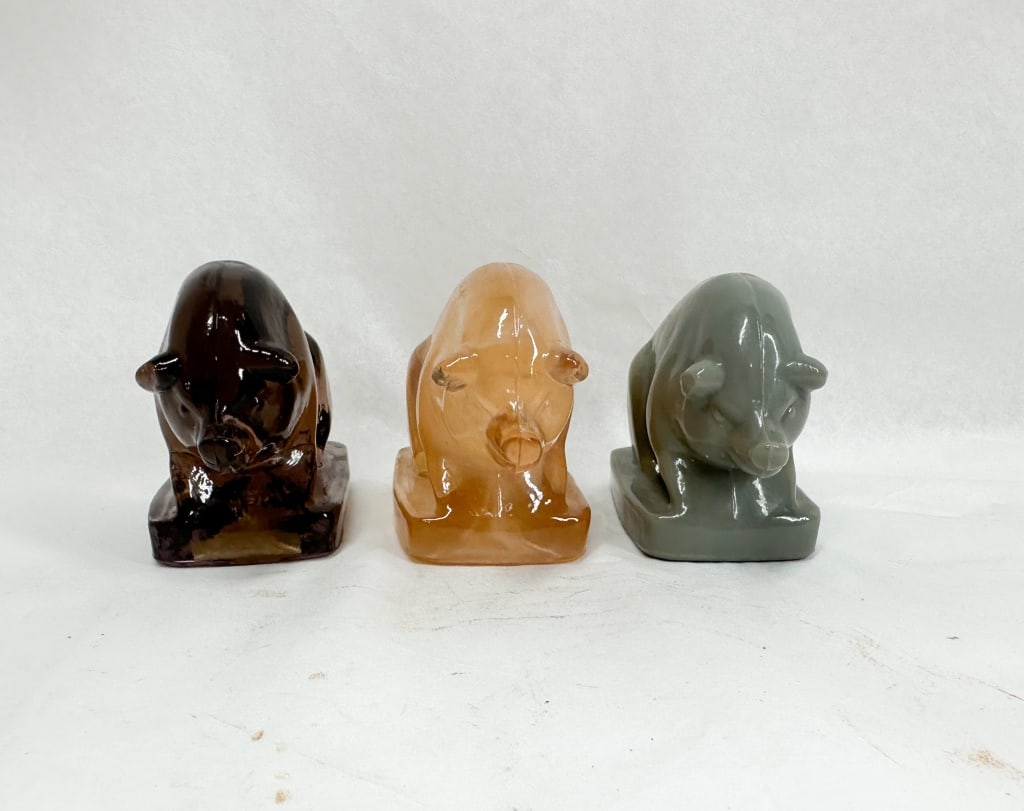 BOYD GLASS SUEE PIG FIGURINES: A trio of seated pig figurines in various colored glass. Each pig features an embossed diamond-shaped mark containing the letter B on the rear haunch, identifying them as Boyd's Crystal Art Glass. The