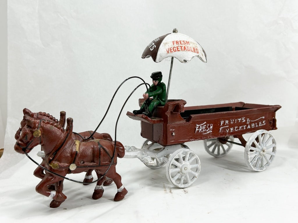 CAST HORSE-DRAWN FRUIT AND VEGETABLE WAGON: Cast iron horse-drawn delivery wagon featuring a pair of brown horses and a maroon-painted cart with a white chassis. The wagon is decorated with a white and brown umbrella and side panels reading FRE