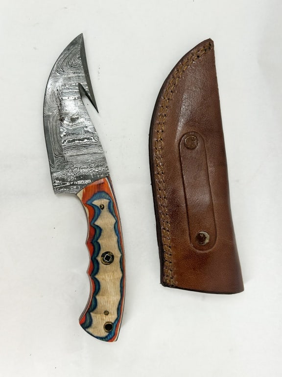 DAMASCUS STEEL GUT HOOK SKINNER: A fixed-blade hunting knife featuring a pattern-welded steel blade with an integrated gut hook. The full-tang handle is fitted with multi-colored laminated wood scales in blue, orange, and natural ton