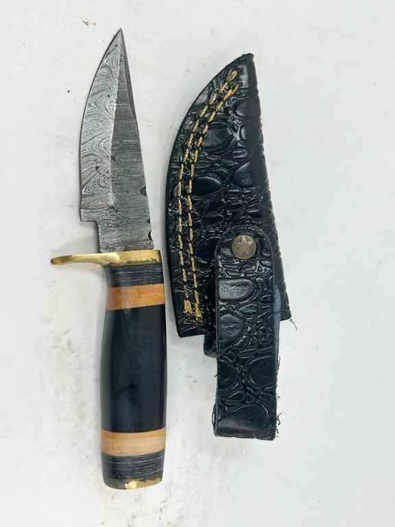 DAMASCUS STEEL HUNTING KNIFE AND SHEATH: A fixed-blade hunting knife featuring a pattern-welded Damascus steel blade with a drop-point profile and jimping along the spine. The handle is constructed with a brass crossguard and pommel, featuri