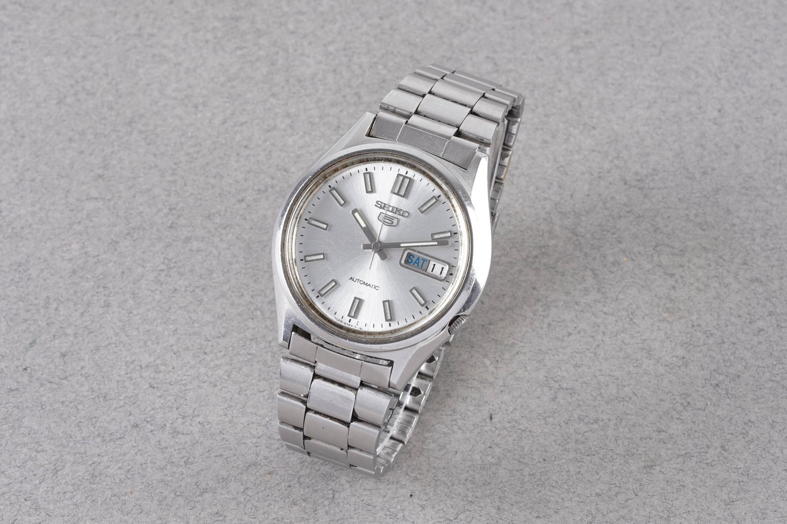 SEIKO 5 DAY DATE AUTOMATIC REF. 7009-8980: SEIKO 5 DAY DATE AUTOMATIC REF. 7009-8980, this watch is a ref. 7009-8980 and is fitted with a circular silver dial with a day date window, applied silver stick hour markers and hands. The 37mm