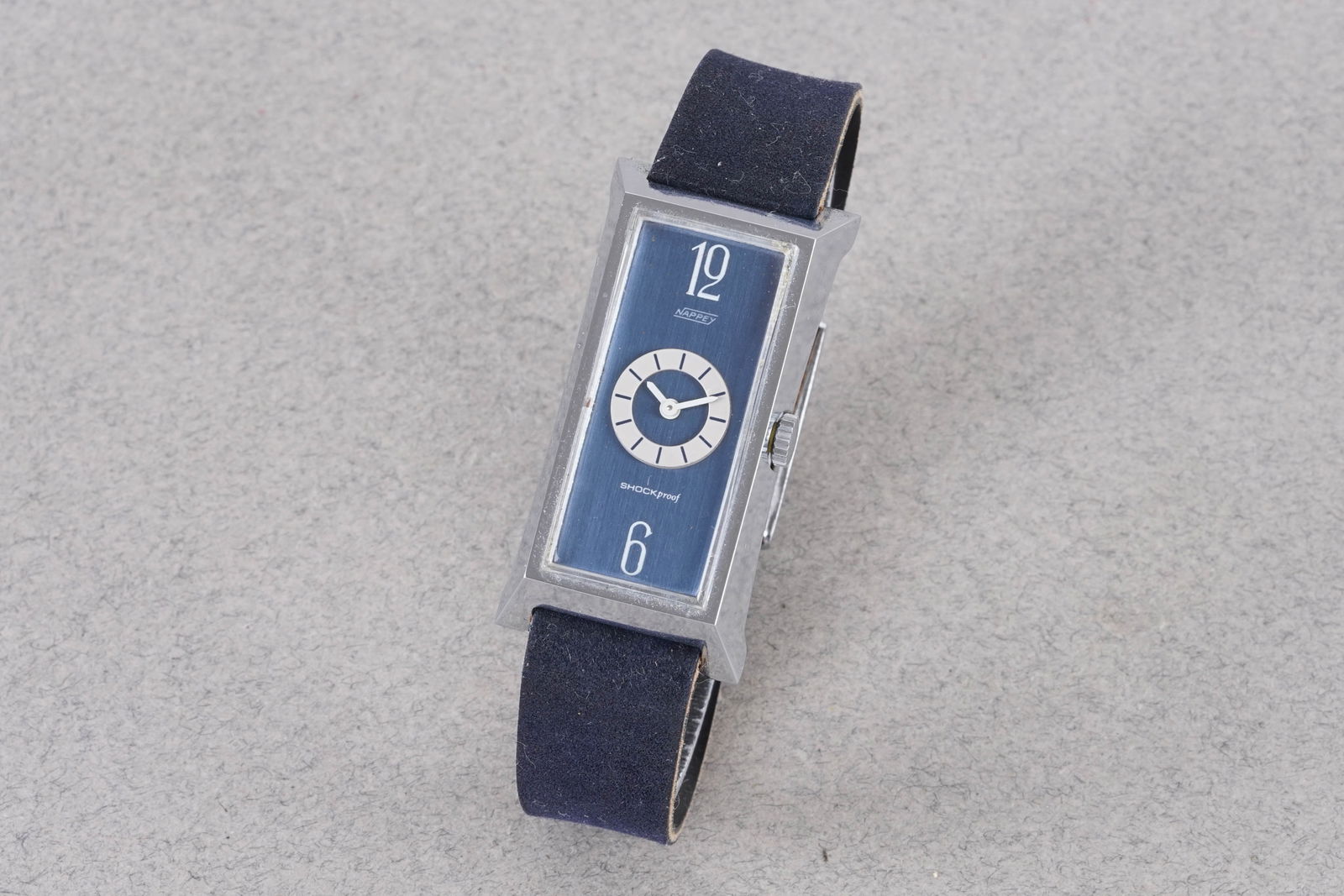 NAPPEY SHOCKPROOF TANK STYLE WRISTWATCH: NAPPEY SHOCKPROOF TANK STYLE WRISTWATCH, this watch is fitted with a rectangular blue dial with hour markers and hands. The 21x45mm case is fitted with a crown and a case back. Inside is a manually