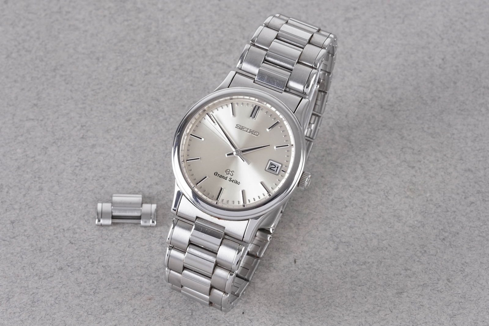 GRAND SEIKO DATE W/ EXTRA LINKS REF. 9587-7010: GRAND SEIKO DATE W/ EXTRA LINKS REF. 9587-7010, this watch is a ref. 9587-7010 and is fitted with a circular silver dial with stick hour markers and hands. The 34mm stainless steel case is fitted with