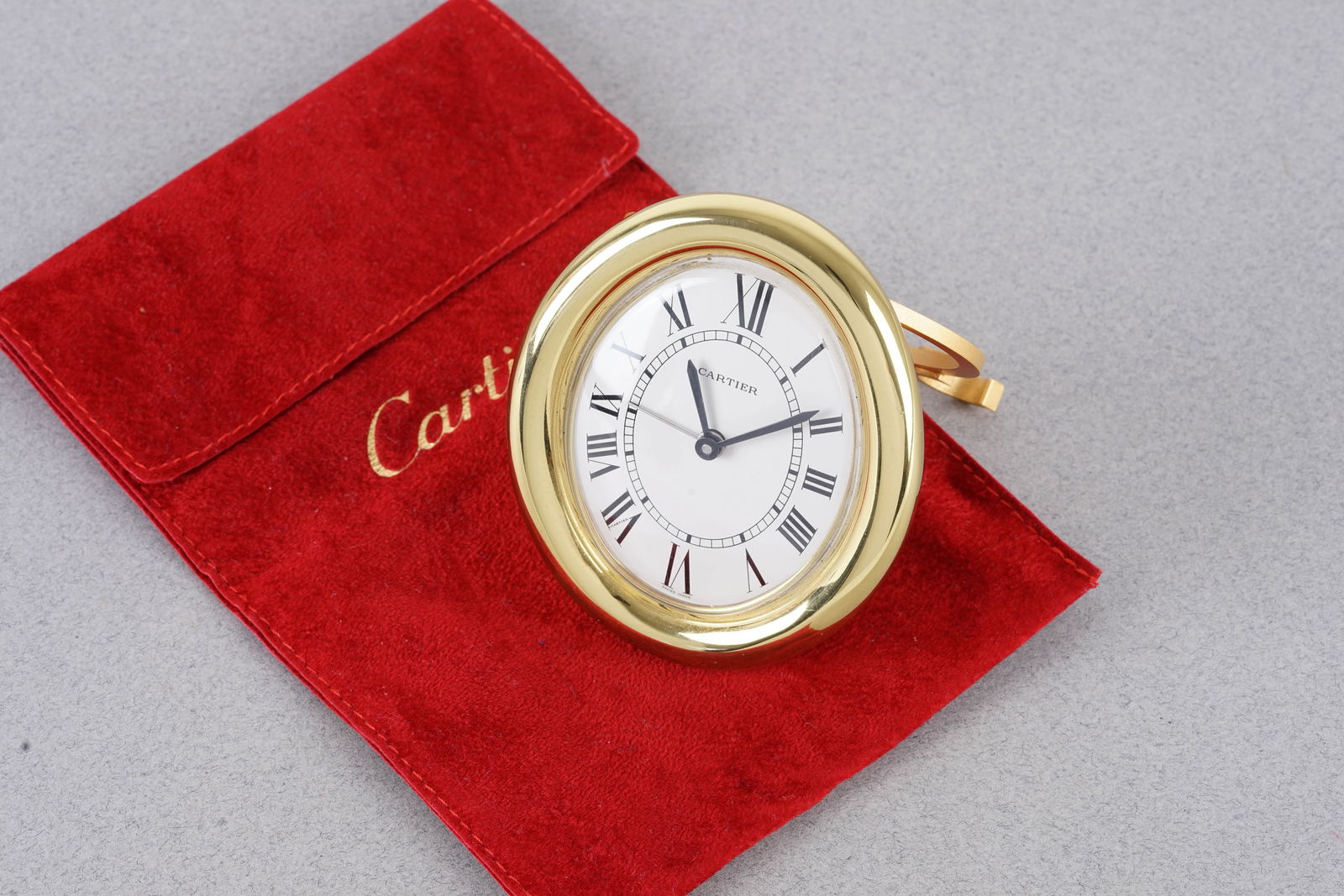 CARTIER DESK CLOCK W/ TRAVEL POUCH: CARTIER DESK CLOCK W/ TRAVEL POUCH, this watch is fitted with a oval dial with roman numeral hour markers and hands. The 75x90mm case is fitted with a crown and a case back. Inside is a quartz