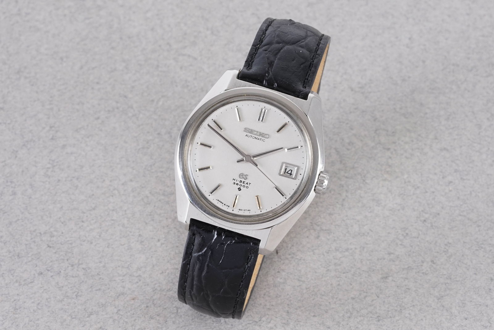 GRAND SEIKO AUTOMATIC DATE REF. 6145-8000: GRAND SEIKO AUTOMATIC DATE REF. 6145-8000, this watch is a ref. 6145-8000 and is fitted with a circular silver dial with a date window, applied stick hour markers and hands. The 37mm stainless steel c