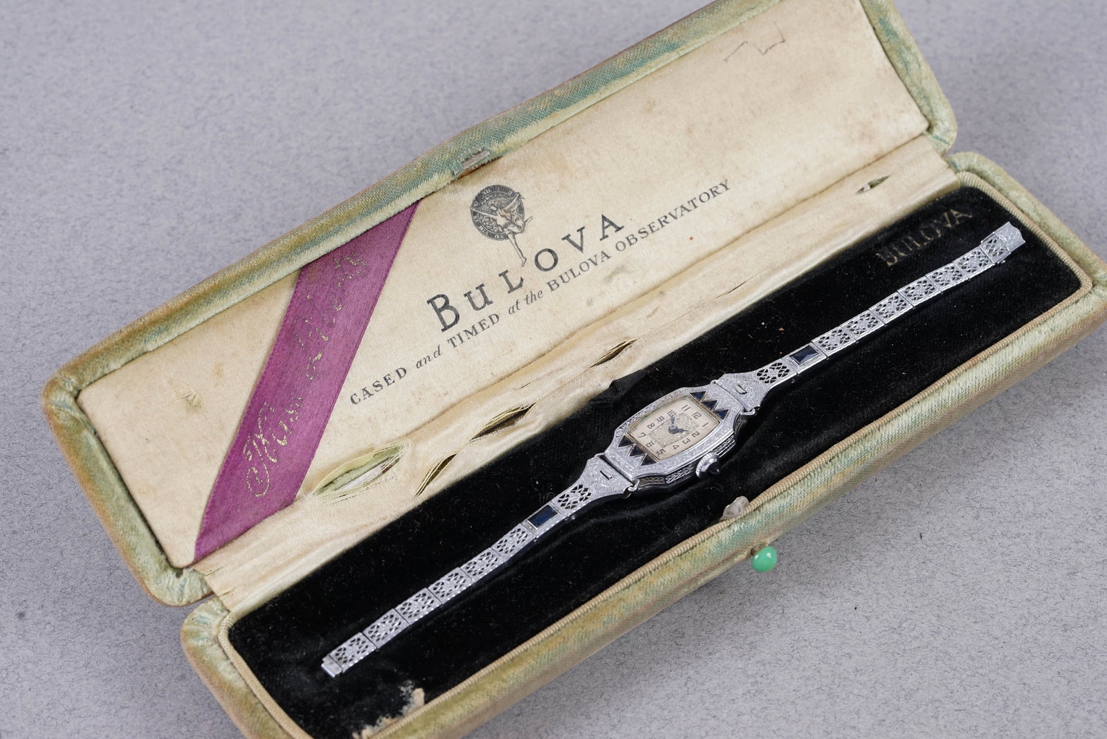 BULOVA SAPPHIRE SET COCKTAIL WATCH W/ BOX: this watch is fitted with a oblong dial with numbered hour markers and antique blue hands. The 17 mm steel case is fitted with a sapphire crown and a snap case back. Inside is a manual movement which