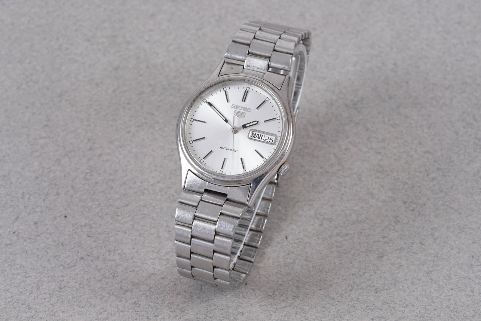 SEIKO 5 DAY DATE AUTOMATIC REF. 7S26-3100: SEIKO 5 DAY DATE AUTOMATIC REF. 7S26-3100, this watch is a ref. 7S26-3100 and is fitted with a round white dial with a day/date window, baton hour markers and hands. The 35 mm steel case is fitted wit