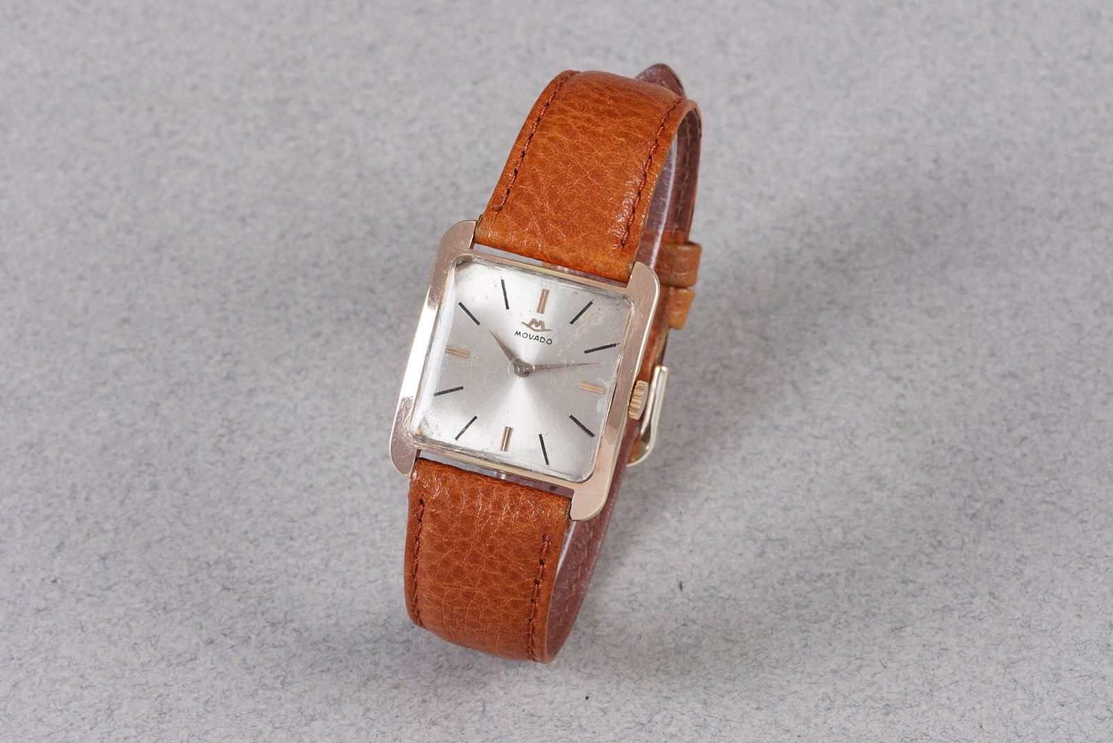 MOVADO CIOCCOLATONE ROSE GOLD PLATED WRISTWATCH: MOVADO CIOCCOLATONE ROSE GOLD PLATED WRISTWATCH, this watch is fitted with a square patina dial with stick hour markers and hands. The 33.5mm gold plated case is fitted with a crown and a case back.