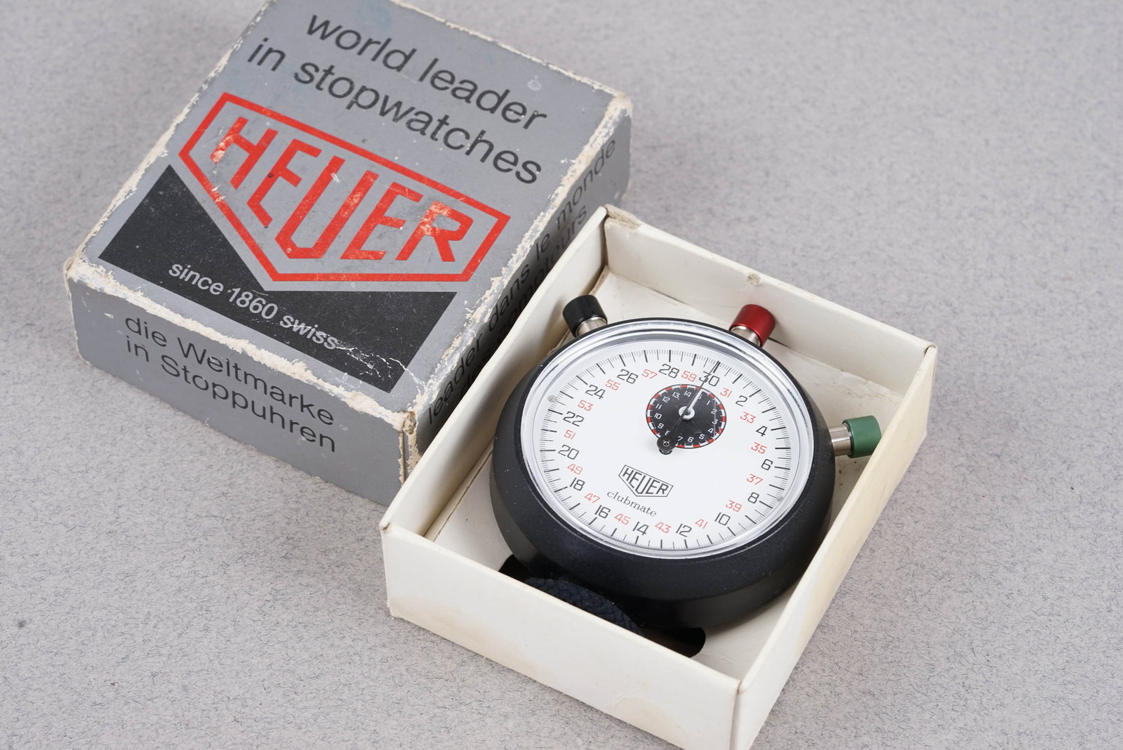 HEUER CLUBMATE TIMER W/ BOX: HEUER CLUBMATE TIMER W/ BOX, and is fitted with a circular white dial with with black sub dial. The 60mm plastic case is fitted with 3 stop, start, reset buttons. Inside is a manual movement which is
