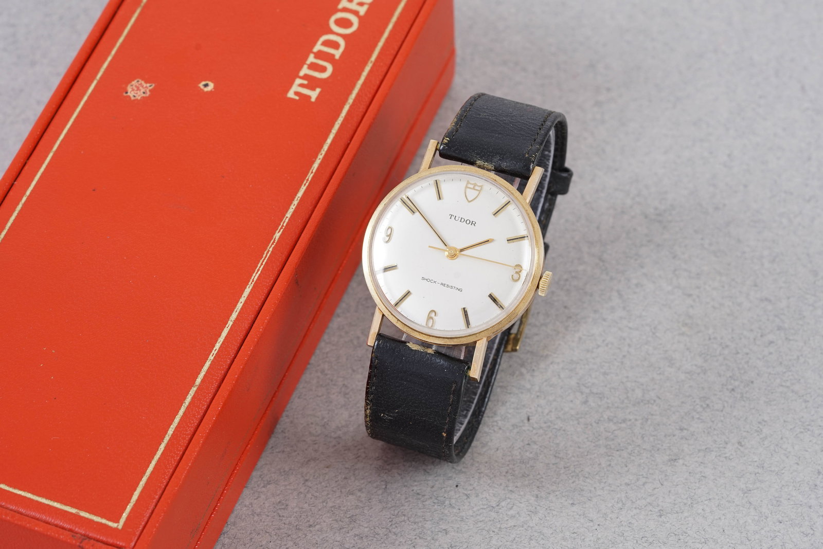 TUDOR 9CT GOLD CHOCK RESISTING W/ BOX: This watch is fitted with a round white dial with baton and number hour markers with baton hands. The 35 mm 9ct gold (with inscription to the back) case is fitted with a crown and a snap case back. In