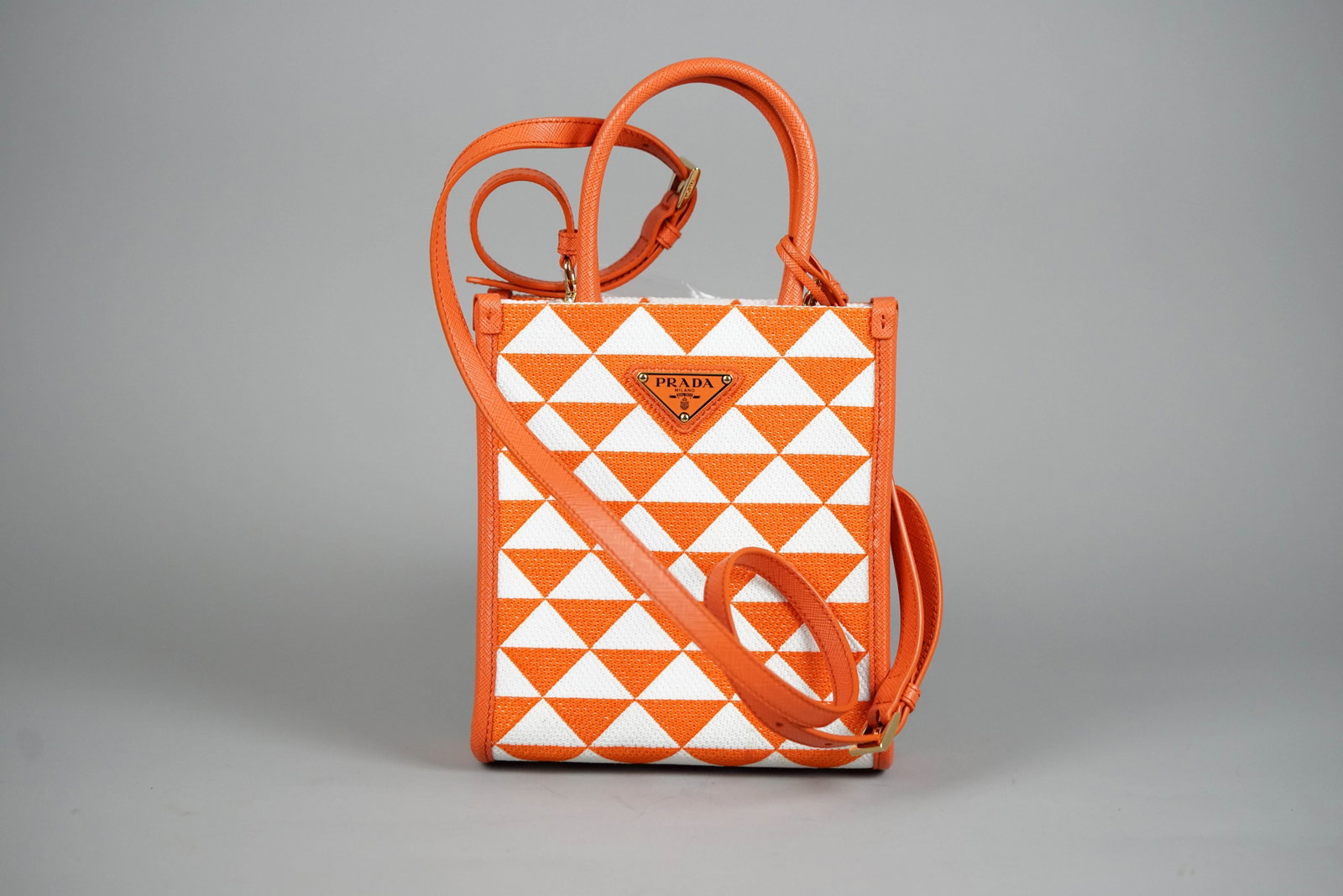 PRADA SYMBOL HANDBAG CANVAS LEATHER RFID TWO-TONE SHOULDER STRAP CROCHET: PRADA SYMBOL HANDBAG CANVAS LEATHER RFID TWO-TONE SHOULDER STRAP CROCHET DIMENSIONS: Width 16.5cm, height 20cm, depth 7cm COLOUR: Red/orange and white ACCESSORIES: Guarantee card, dust bag CONDITION R