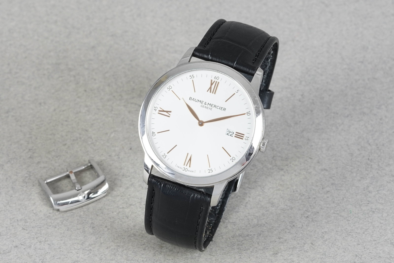 BAUME & MERCIER GENEVE DATE CLASSIMA WRISTWATCH: BAUME & MERCIER GENEVE DATE CLASSIMA WRISTWATCH DIAL: Circular silver off white dial, date window, gold tone hour markers CASE: 42mm stainless steel MOVEMENT: Quartz BRACELET OR STRAP: Leather