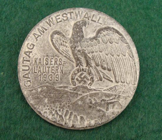 1939 GAUTAG AT WESTWALL BADGE, KAISERSLAUTERN ORIG: LARGE GAU TAG AT WEST WALL KAISERSLAUTERN BADGE. 1 3/4" IN DIAMETER. SHOWS EAGLE/SWASTIKA OVER WESTWALL. REVERSE MARKED "RZM M9/56 -WERNER REDO SAARLAUTERN AND ADDL MAKR MARK. 1 3/4" IN DIAMETER. EXCE
