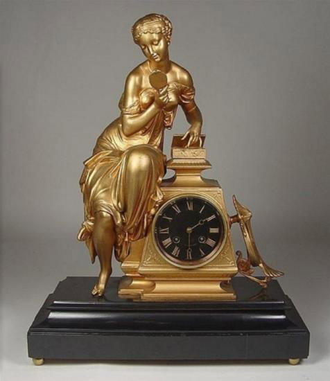 French Gilt Figural Clock: French Gilt Figural Clock, _Circa 1870. Black enamel Roman dial with gilt numerals, in obelisk base with figure of maiden with mirror and dressing box. 20" x 16" x 7".