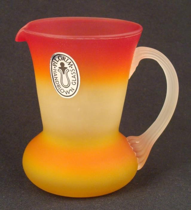 Pilgrim Hand Blown Glass Small Pitcher Tangerine Hue: This is a small Pilgrim Glass pitcher. It is all hand blown, in a tangerine color in striated pattern, with frosted grooved handle. It measures 4" tall, and 4" from handle to spout. Its condition is e