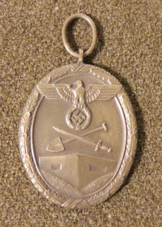 WWII Nazi Westwall Medal Western Front: This is an original WWII era Nazi Westwall Medal. The design shows crossed sword and shovel, with eagle and swastika bordered by oak leaf wreath. The reverse side has the words: FUR ARBEIT ZUM SCHUTZE