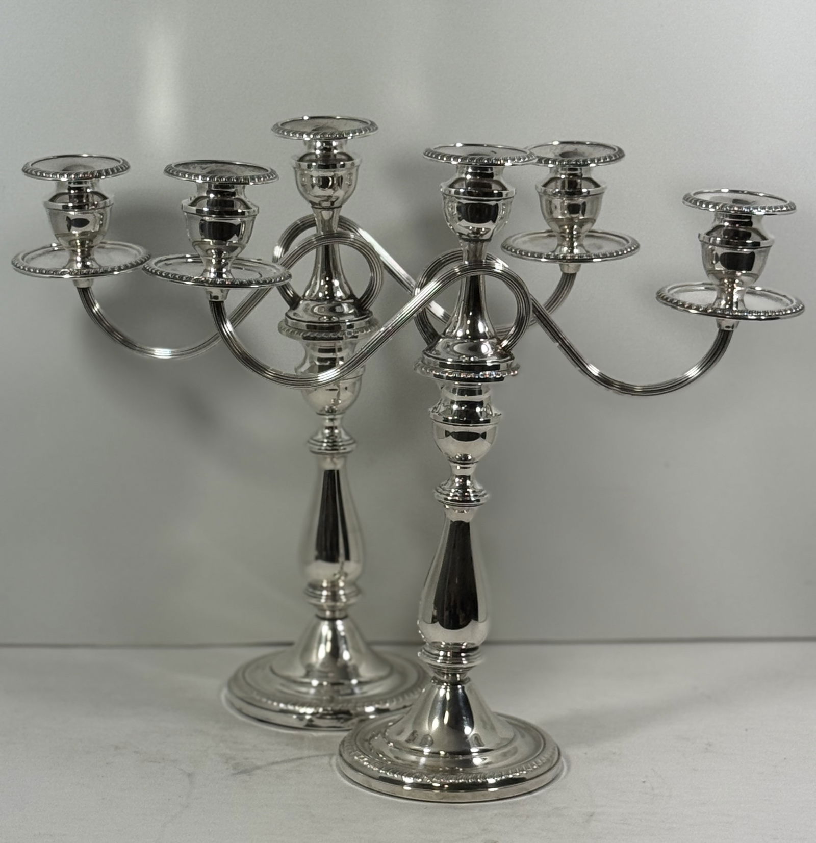 Sterling Silver Convertible Candelabra Pair: Pair of American Sterling Silver convertible candelabra, each with detachable three-light branches. The design allows for versatility: used as tall single candlesticks or fitted with the scrolling thr