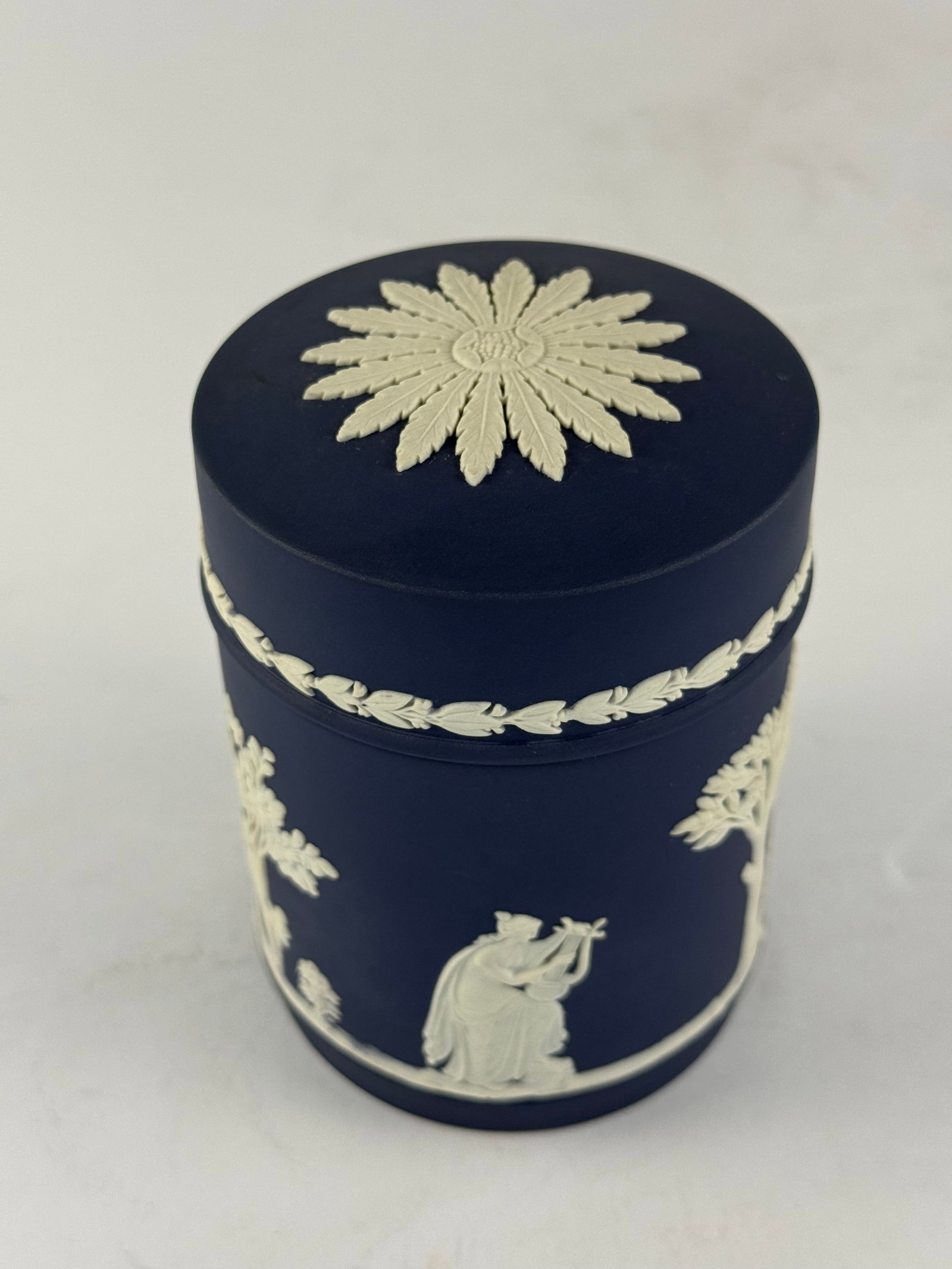 Wedgwood Jasperware Lidded Canister: A refined and authentic Wedgwood Jasperware lidded canister, executed in the iconic matte cobalt blue ground with applied white classical relief decoration. The cylindrical form is adorned with neocla