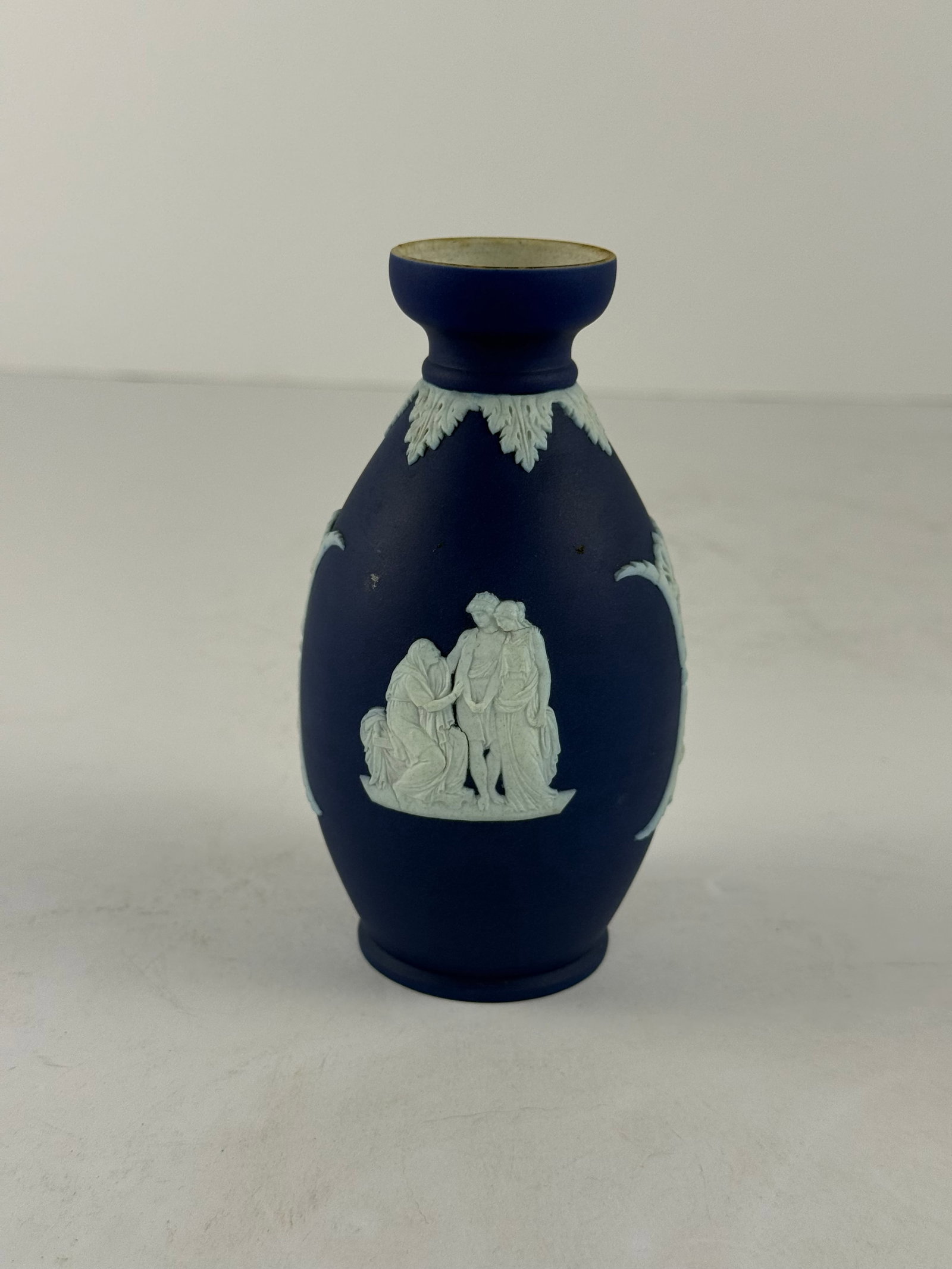 Small Wedgwood Jasperware Vase: A finely modeled small Wedgwood Jasperware vase, rendered in the iconic matte cobalt blue ground with applied white neoclassical relief decoration. The ovoid form is adorned with classical figural sce