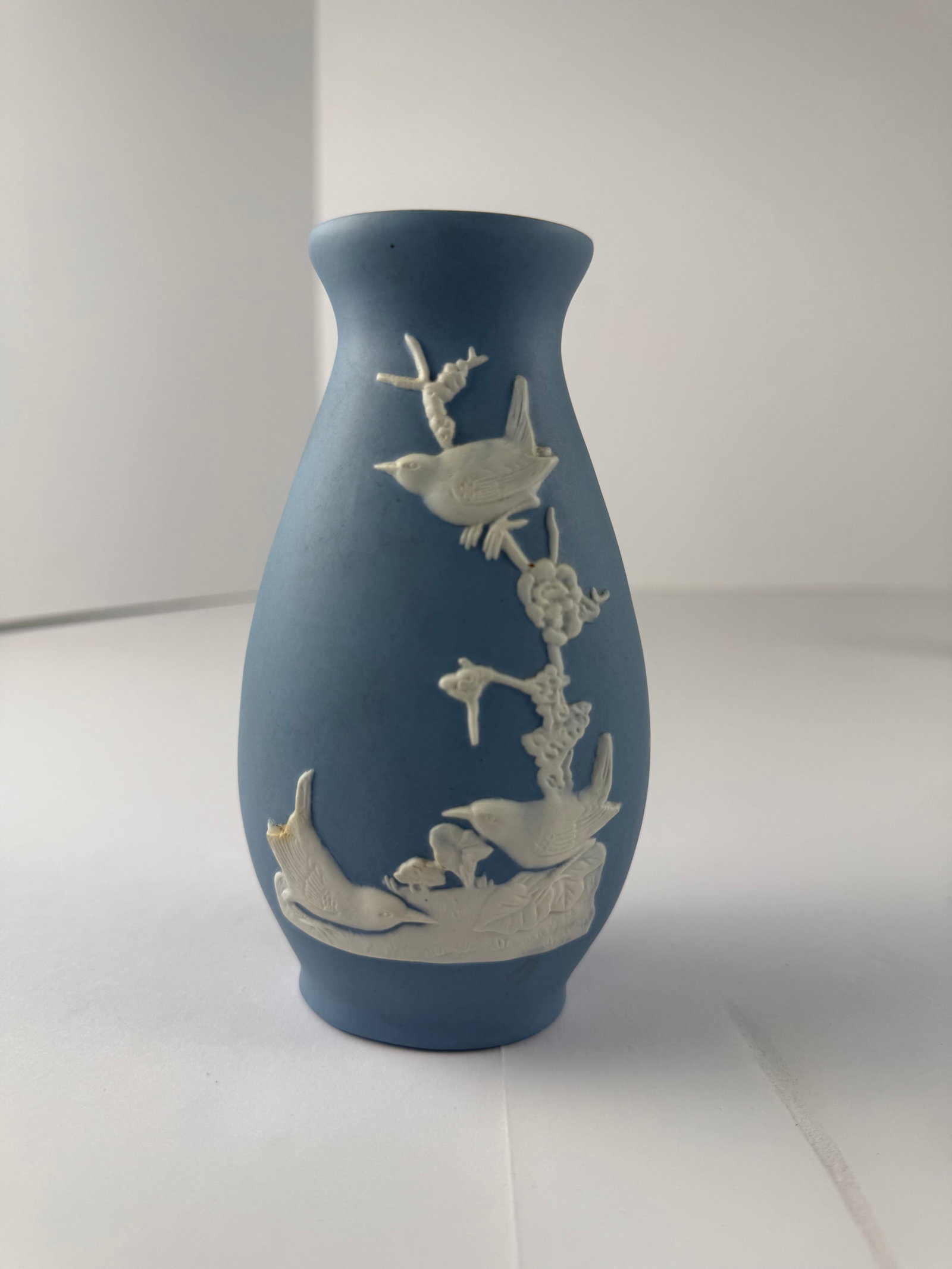 Blue Jasperware Style Vase with Bird Relief: A blue jasperware-style vase featuring applied white relief decoration of birds perched among flowering branches. Rendered in the traditional matte blue ground associated with Wedgwood designs, this p