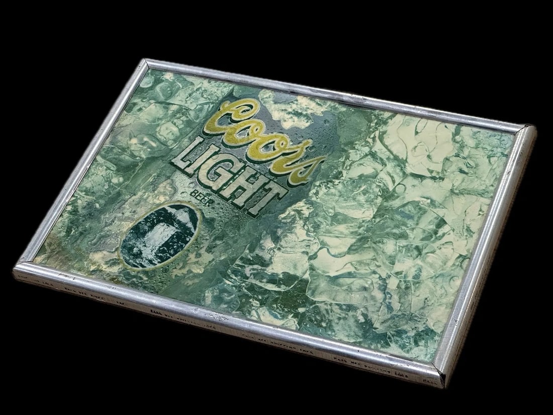 Coors Light Ice-Theme Bar Advertising Display: A Coors Light beer promotional sign with traditional design elements. Silver metal frame housing Coors Light logo against ice-effect background typical of beer advertising imagery. Originally used for