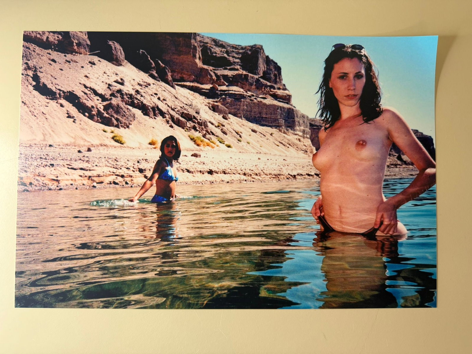 Bunny Yeager – Desert River Nude Study, Hand-Signed Photograph: Original photographic print by legendary American photographer Bunny Yeager, depicting a striking nude figure standing in shallow water within a dramatic desert canyon landscape, accompanied by a seco