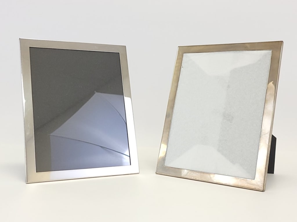 PAIR INMAN STERLING SILVER 7 X 9 PHOTO FRAMES: Pair of Inman sterling silver photo frames for a 7" x 9" photo. Full frame dimensions measure 8" x 10" x .25" thick. Marked on backside at the top. Both backed with black acrylic. Condition: good, no